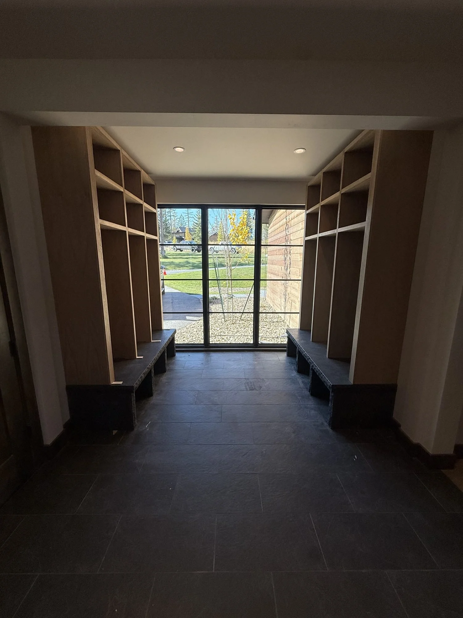 Facing runs of white oak mudroom lockers leading to a glass door