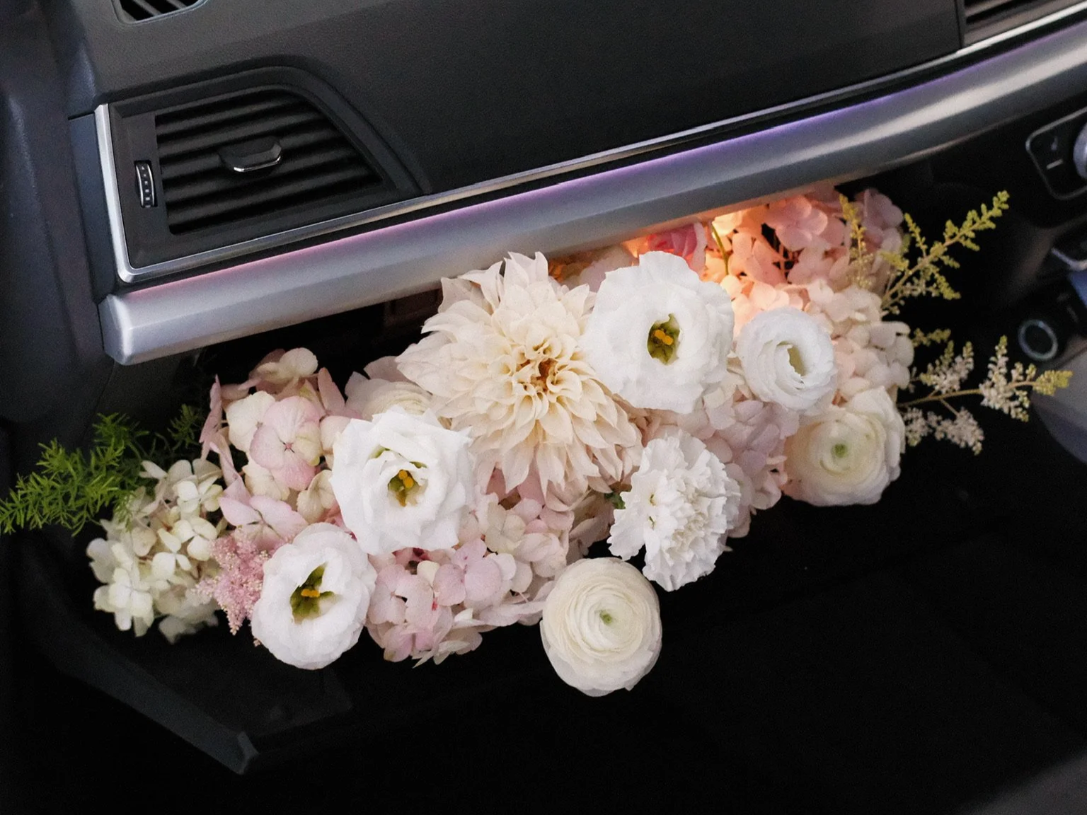 Arrangement of white and light pink flowers placed under a car dashboard.