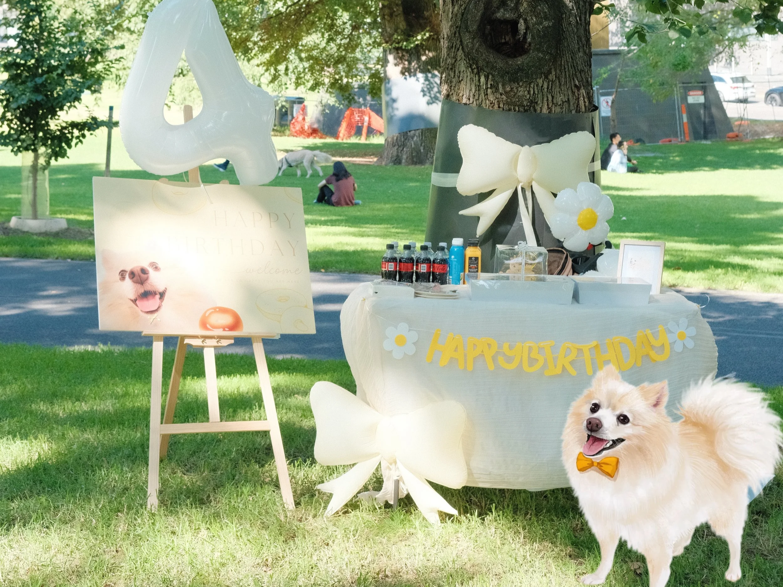Outdoor birthday celebration setup with a table decorated for a dog-themed party, including balloons, a 'HAPPY BIRTHDAY' banner, and a small dog wearing a bowtie and standing on the grass.