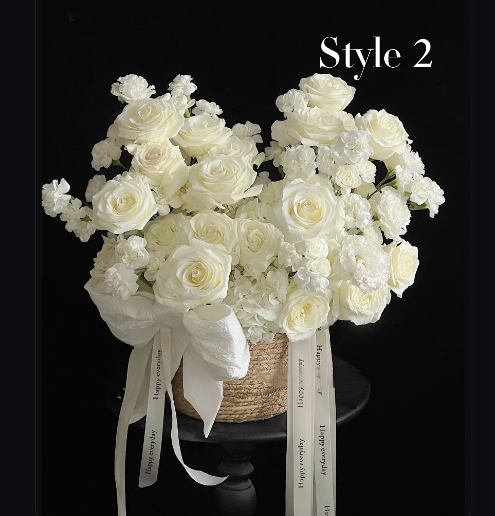 A floral arrangement of white roses and white small flowers in a woven basket, with white ribbons that say 'Happy everyday' tied to it, set against a black background, labeled as Style 2.