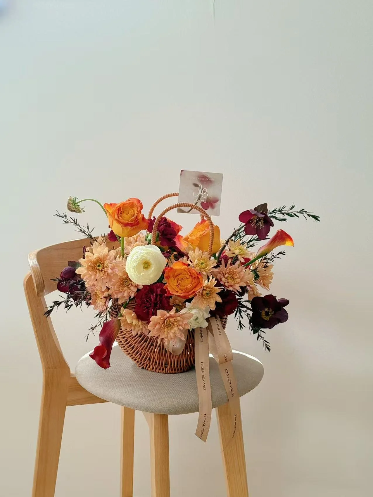 A basket of colorful flowers sitting on a wooden chair with a beige cushion against a plain white wall.