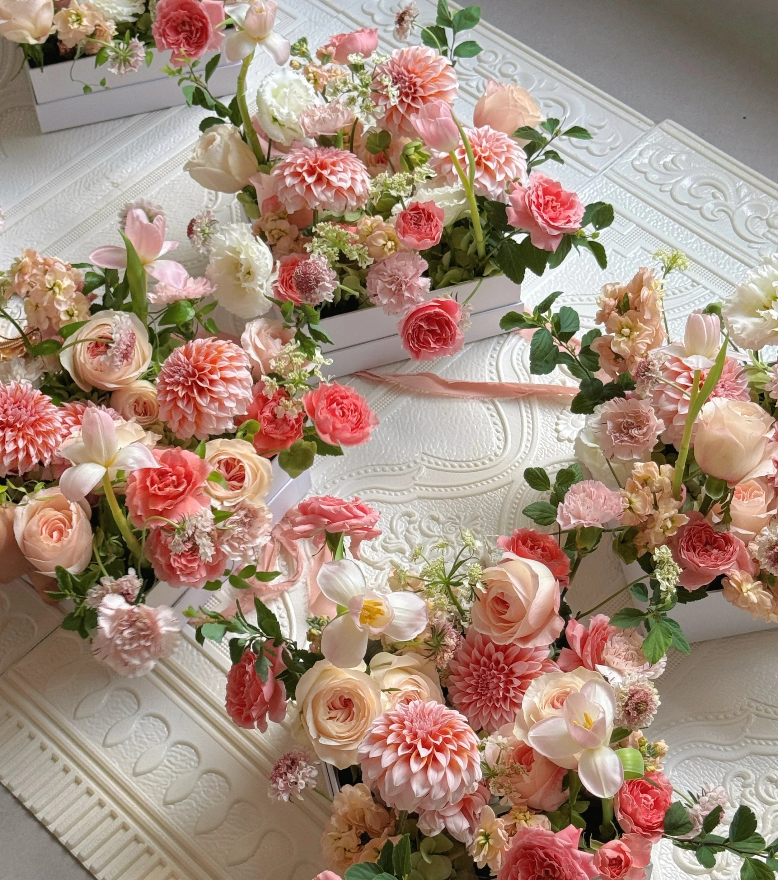 Arrangement of pink and white flowers, including roses, dahlias, and tulips, on a decorative white table.