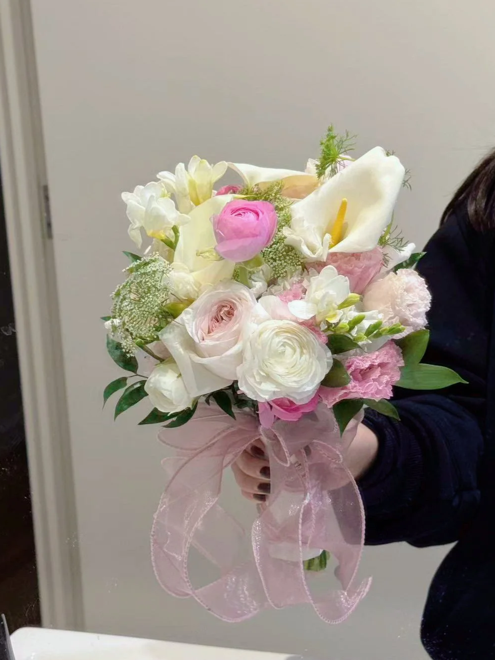 A person holding a bouquet of pink and white flowers with a pink sheer ribbon bow.