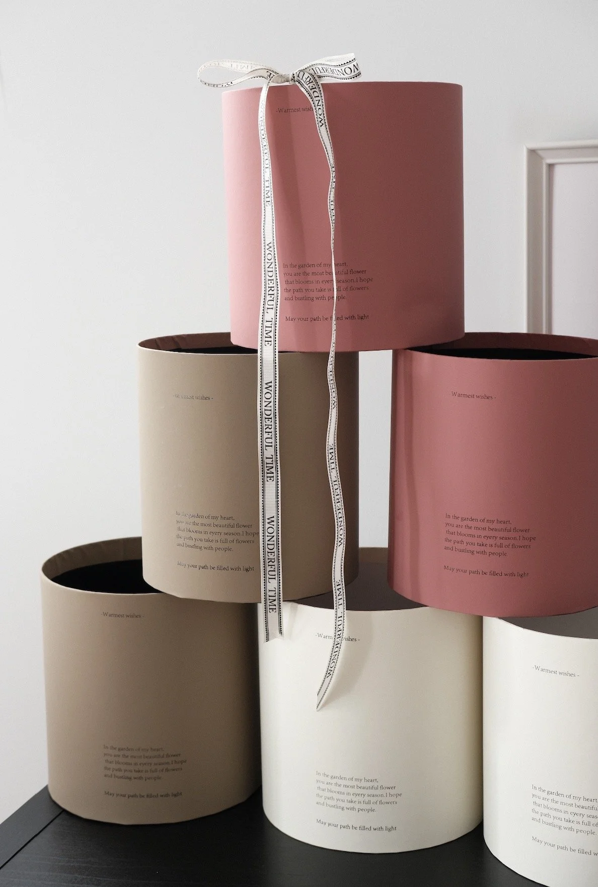 A stack of six round flower boxes with pastel colors, some with text and a ribbon on top.