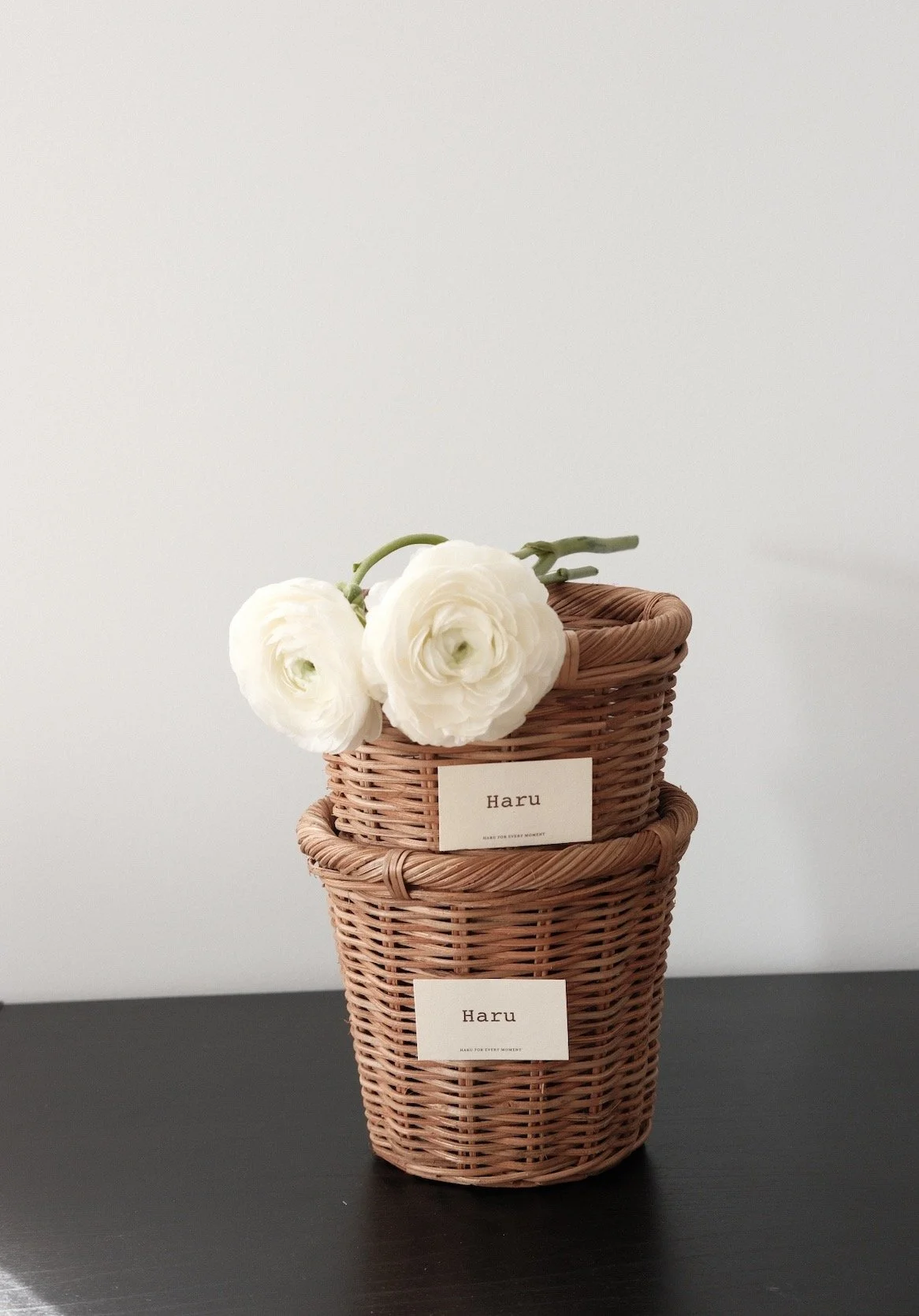 Two stacked woven baskets on a dark surface with white flowers and labels that read "Haru."