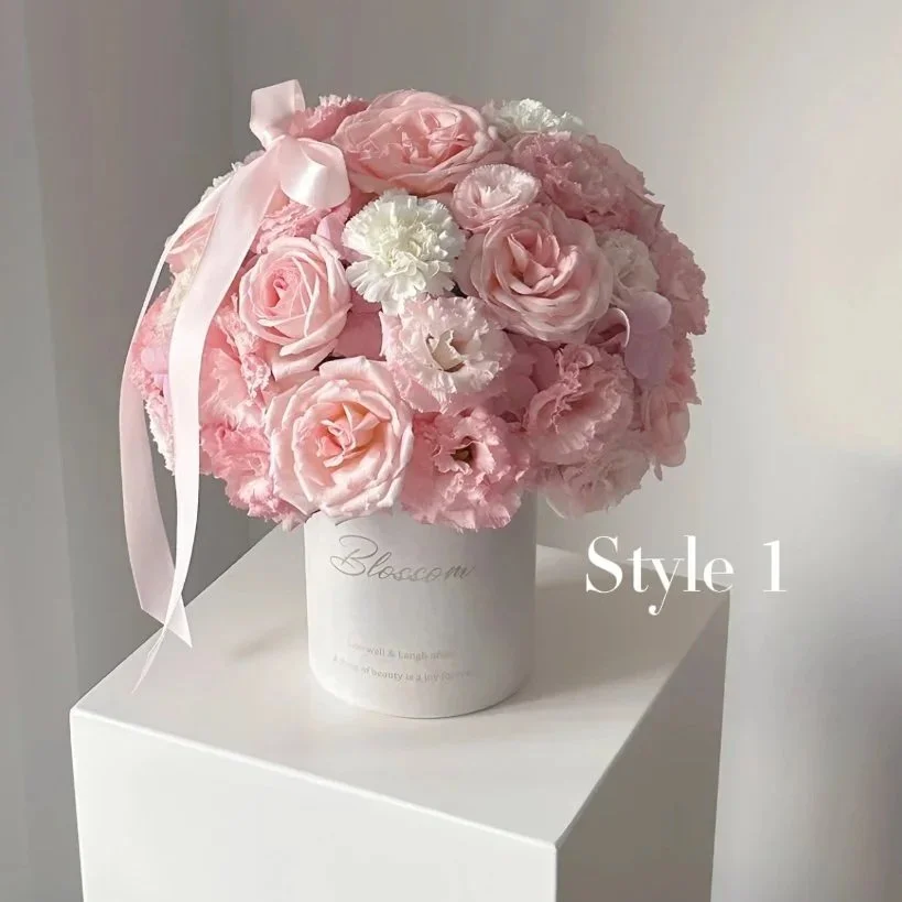 Pink and white flower arrangement in a white vase on a white surface.