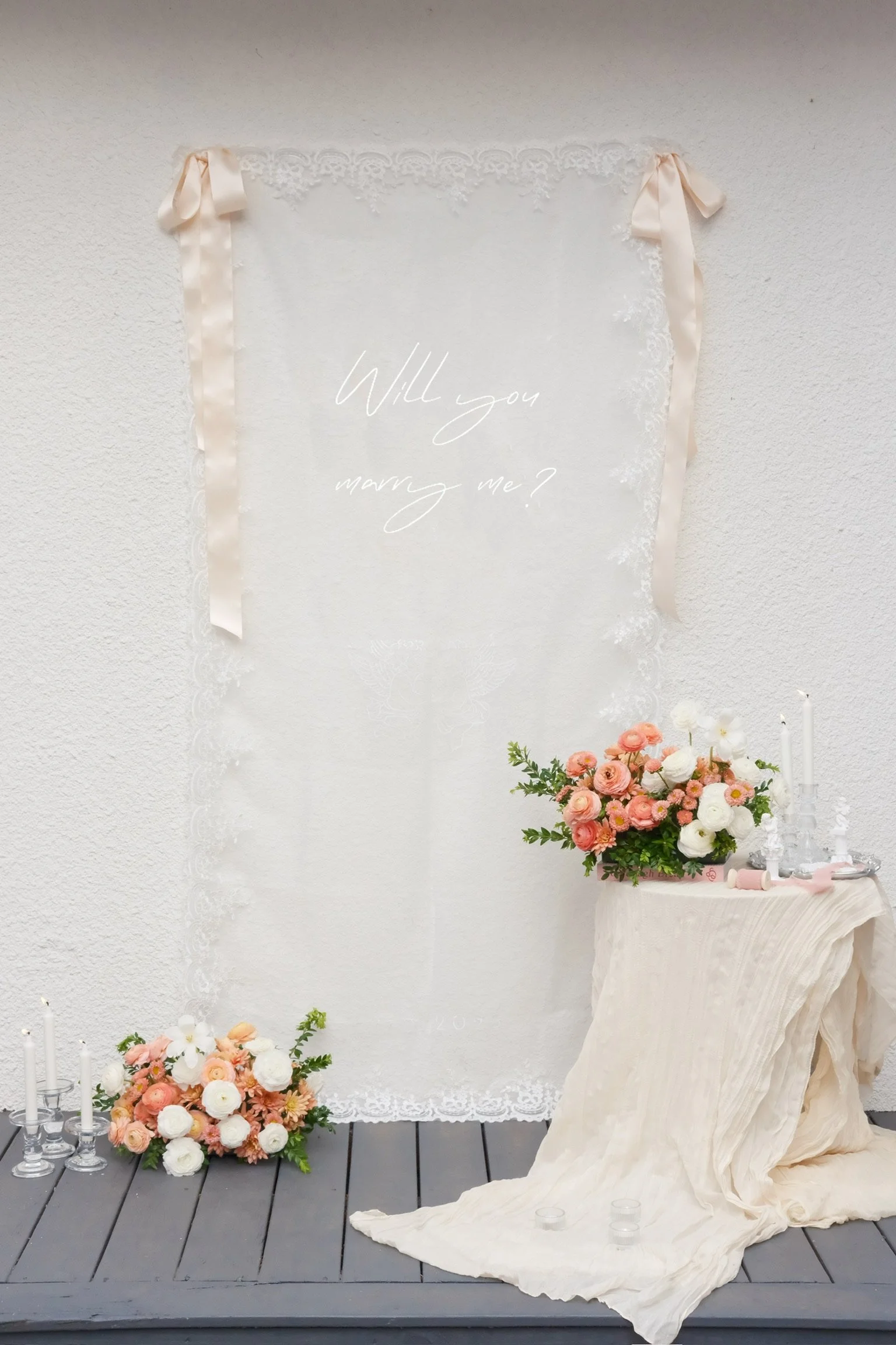 A wedding proposal setup with a sign asking 'Will you marry me?', decorated with flowers, candles, and ribbons.