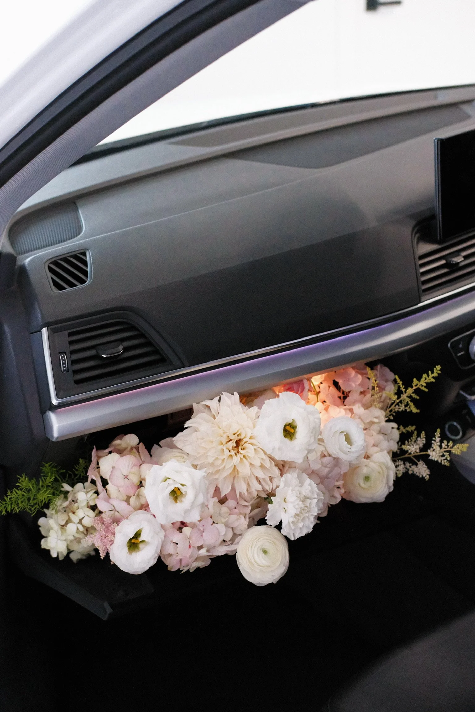 Interior of a car dashboard decorated with a cluster of white, pink, and cream flowers underneath the dashboard.