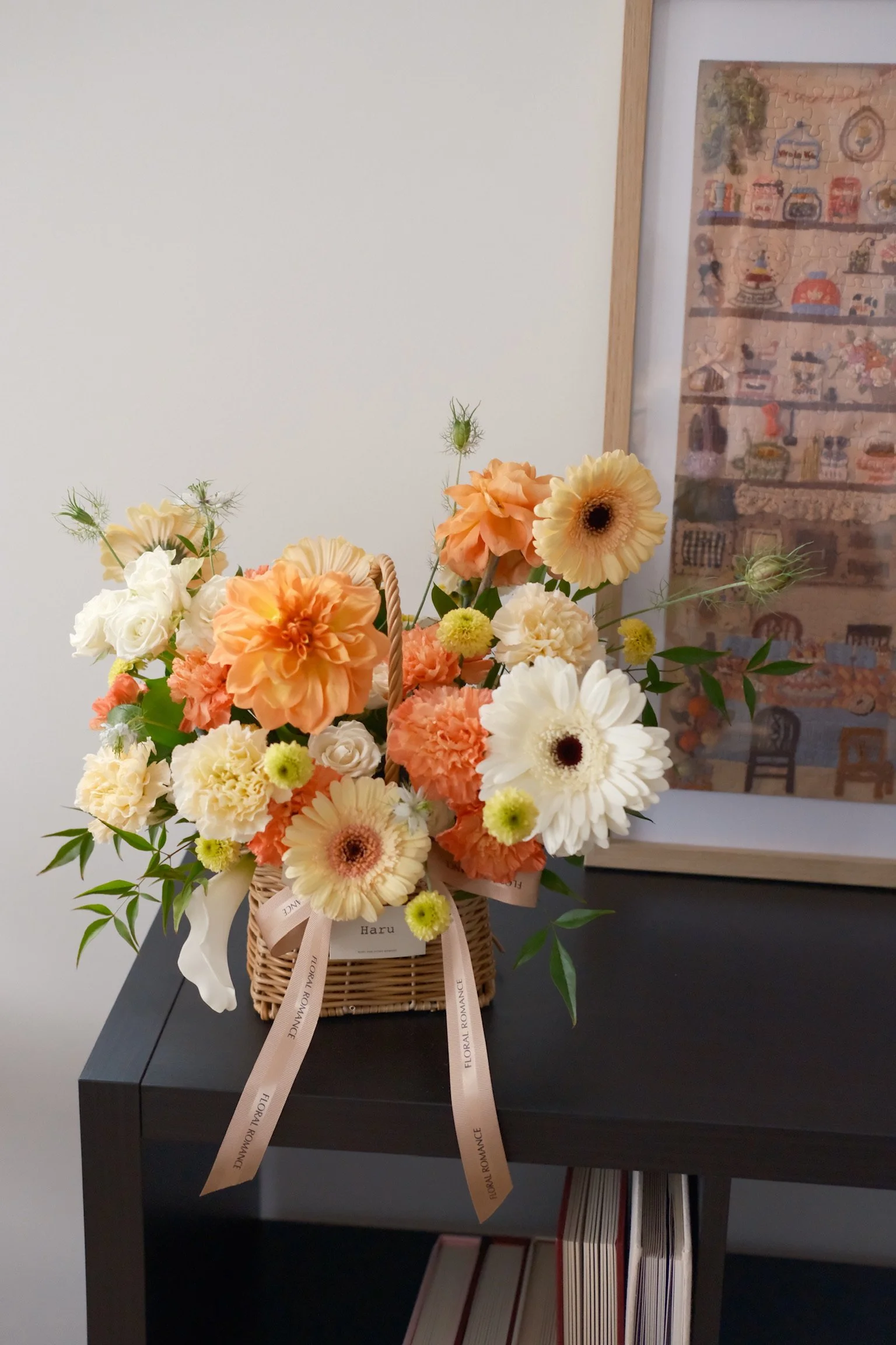 A basket of peach, white, and cream-colored flowers, including daisies and carnations, on a black table.