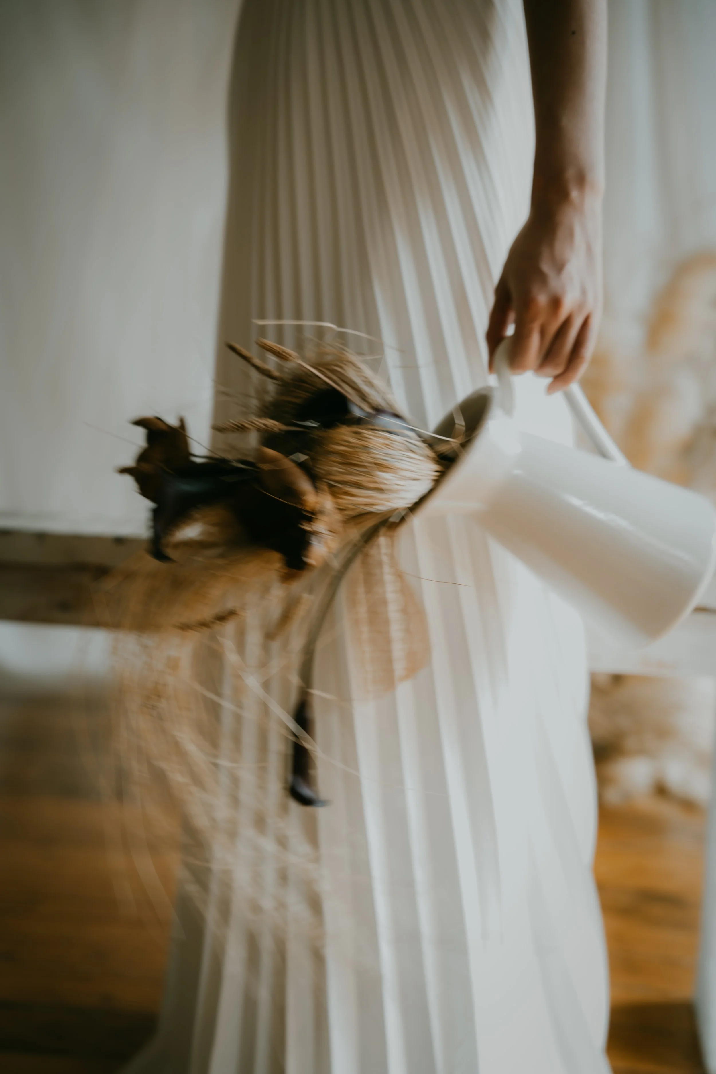 Person pouring flowers from a white pitcher into a vase.