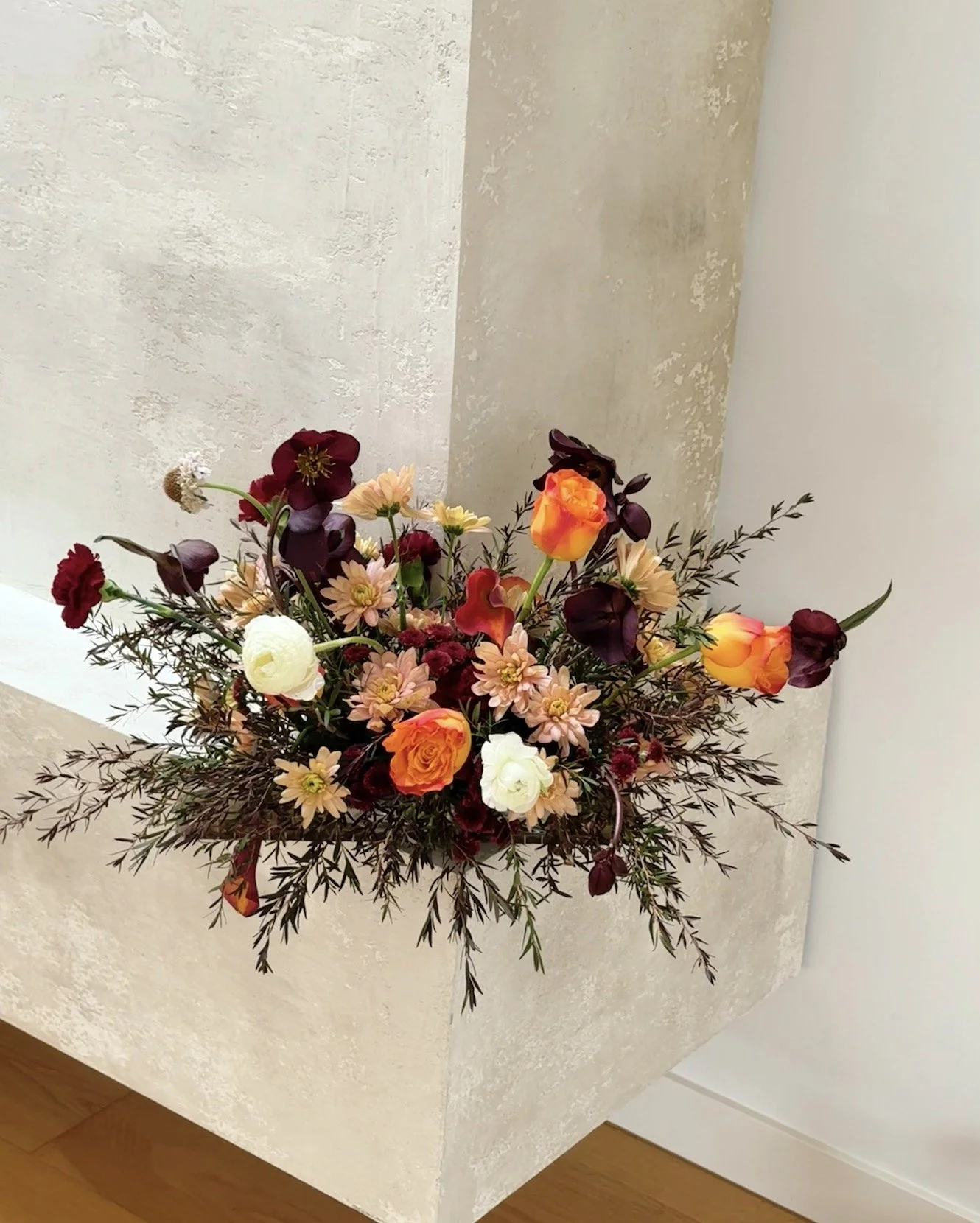 A colorful flower arrangement on a light-colored textured corner surface of a room.
