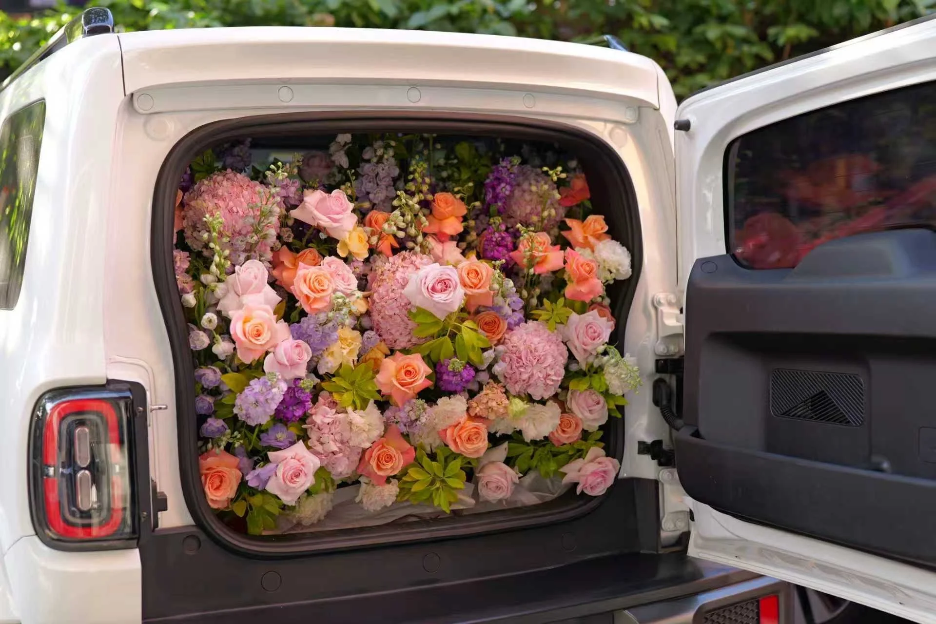SUV with its rear door open, filled with a large assortment of colorful flowers including roses, hydrangeas, and other blossoms.