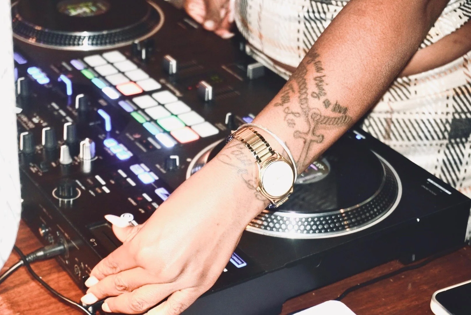 A person with tattoos on their arm using a DJ controller with colorful illuminated buttons and knobs.