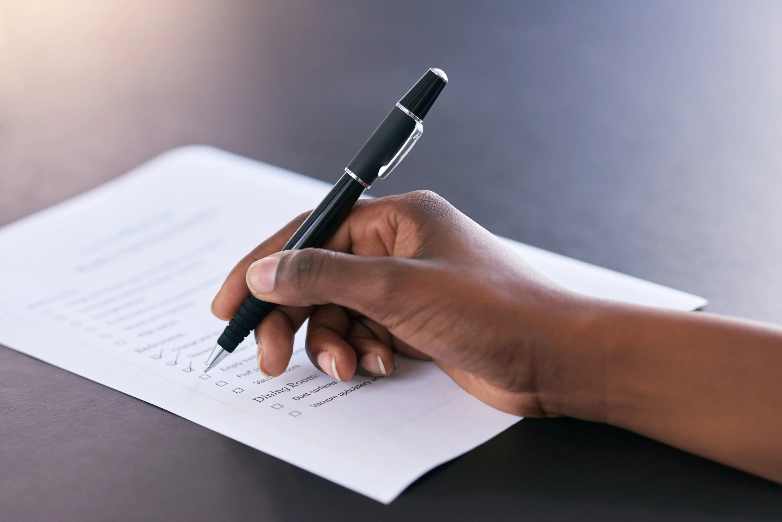 A person filling out a checklist on a piece of paper with a black pen.