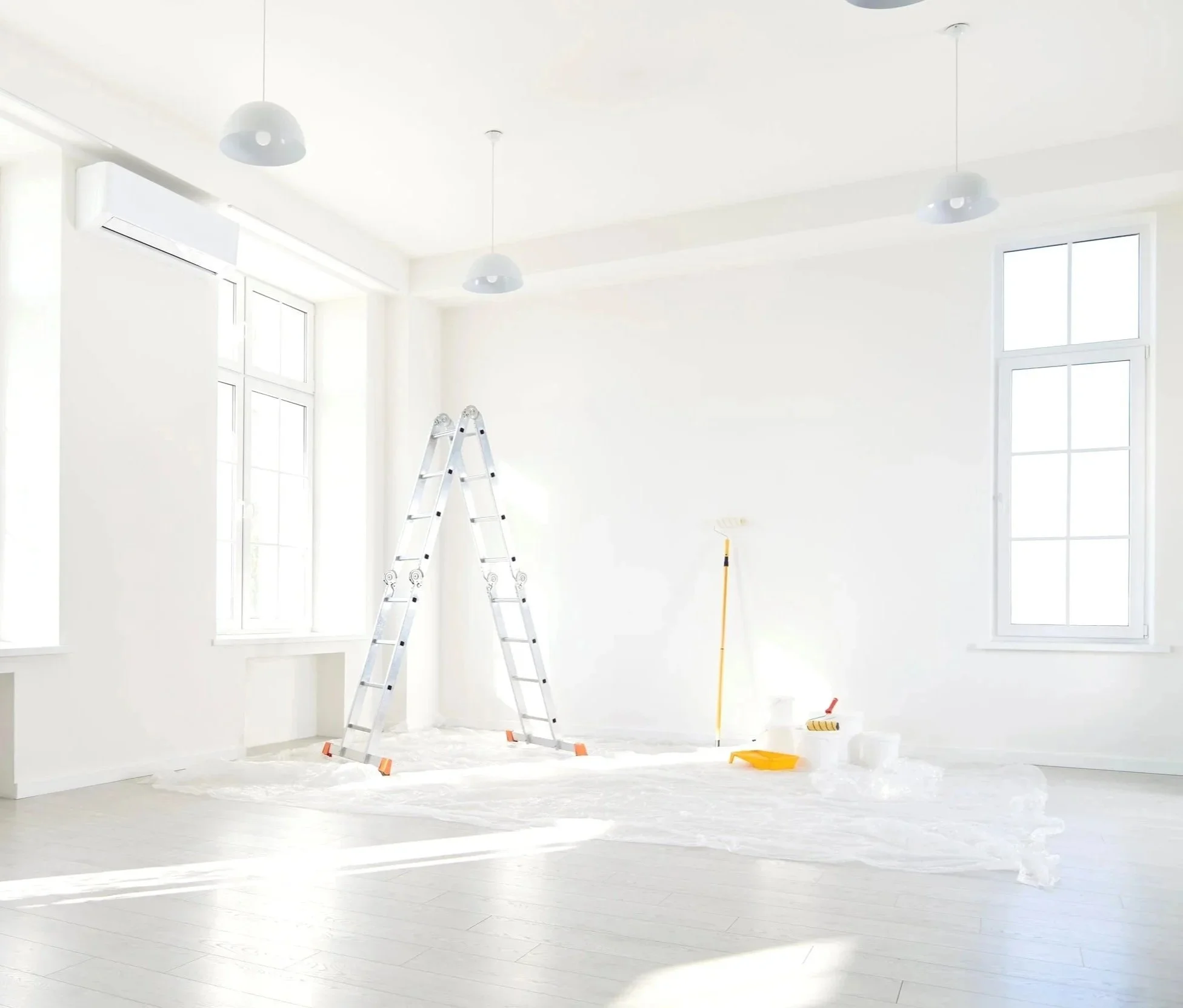 Empty room being painted white with ladders, paint supplies, and plastic covering the floor.