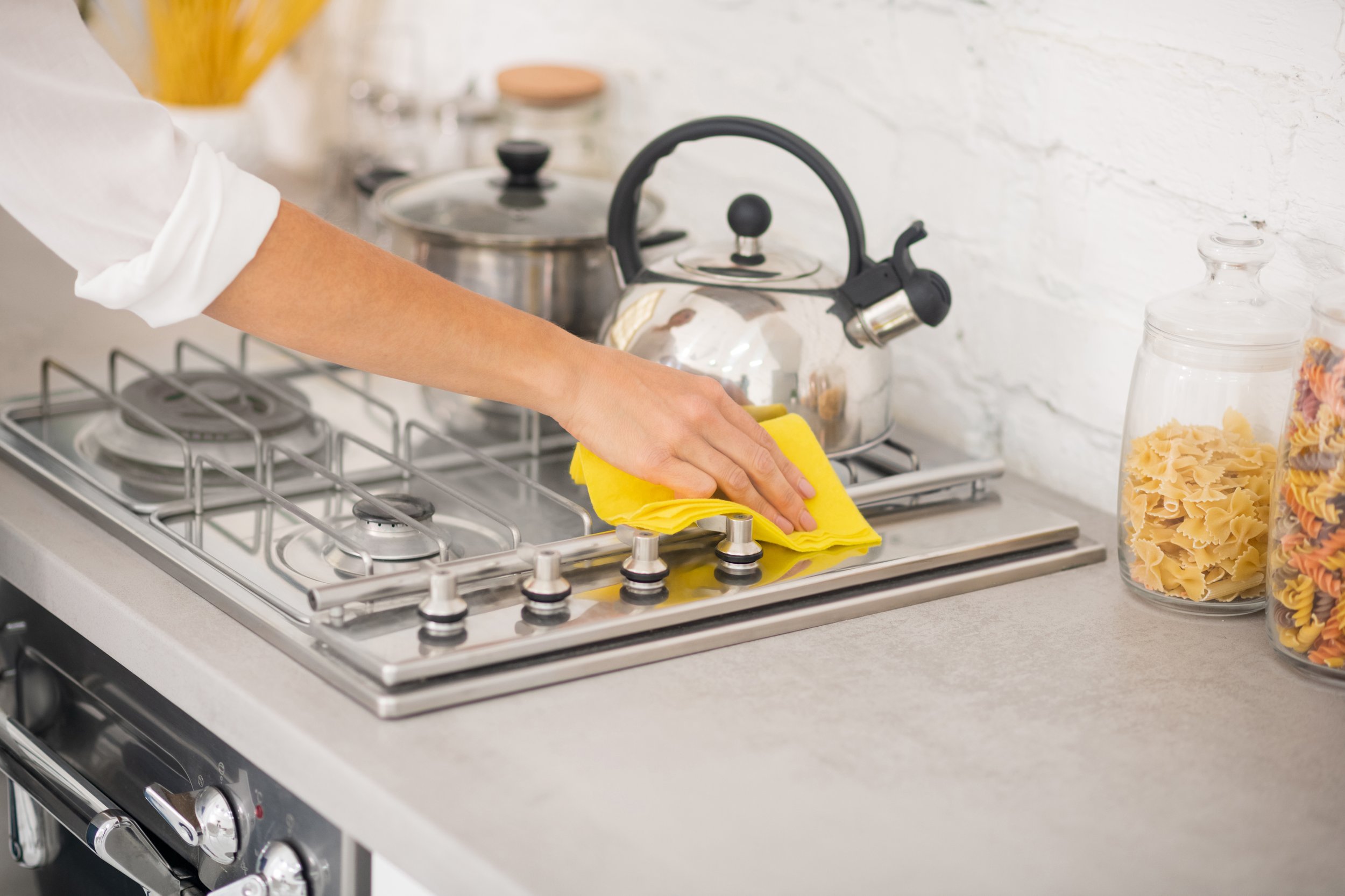 A person cleaning a stovetop with a yellow cloth in a kitchen.
