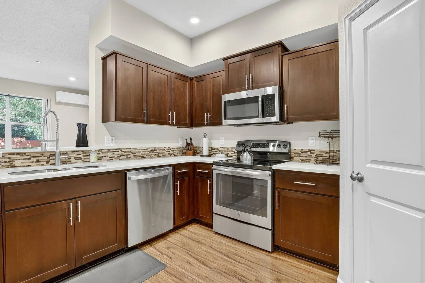 Modern kitchen with dark wood cabinets, stainless steel appliances, a mosaic tile backsplash, and a window above the sink.
