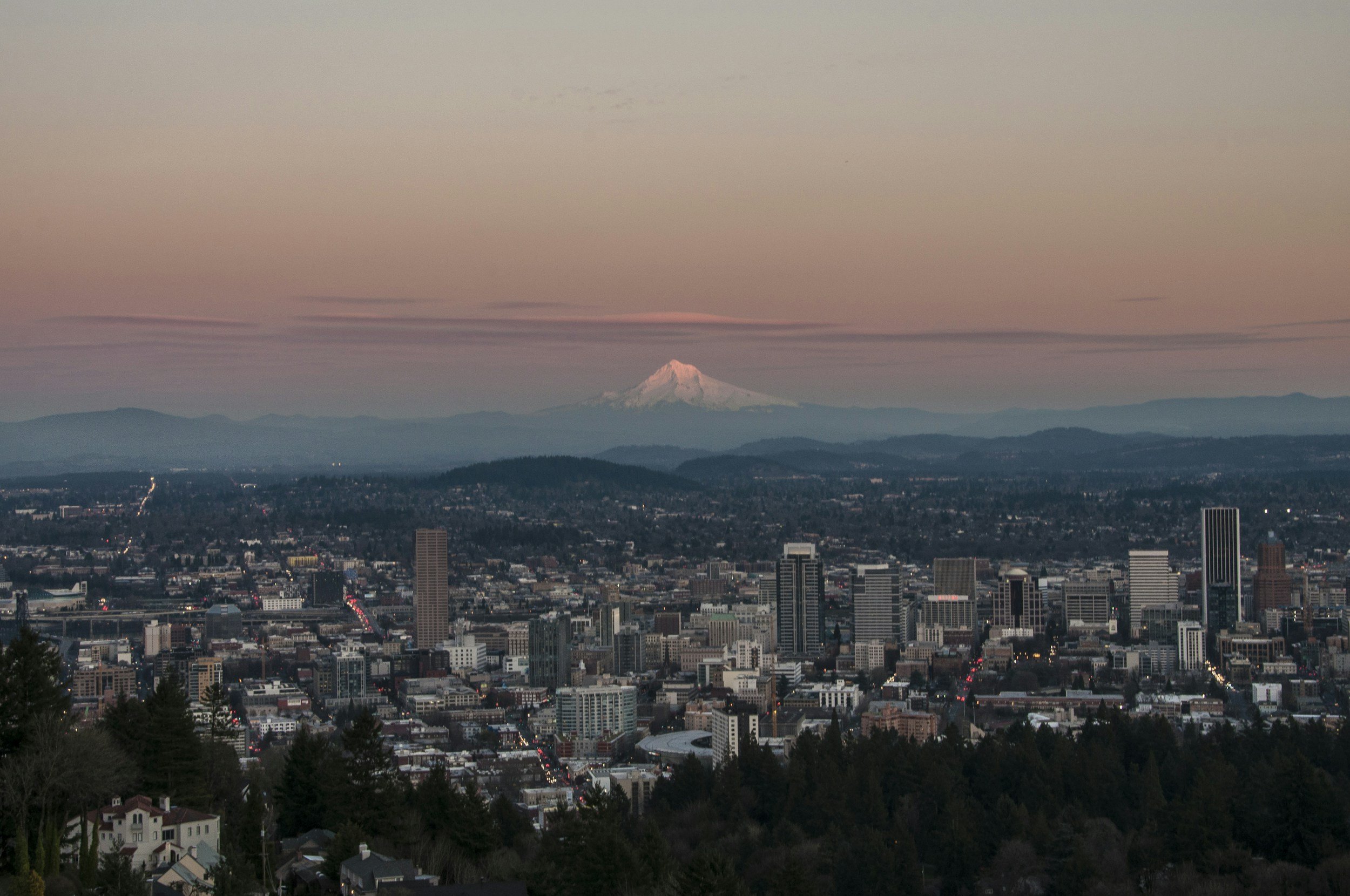 City skyline at dusk with Mount Hood and Mount St. Helens in the background.