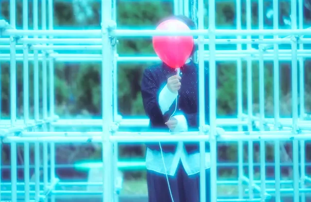 赤い風船を持つ子供が青い光で照らされた遊具の間にいる