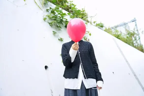 ピンク色の風船を持った人が白い壁の前に立っている。