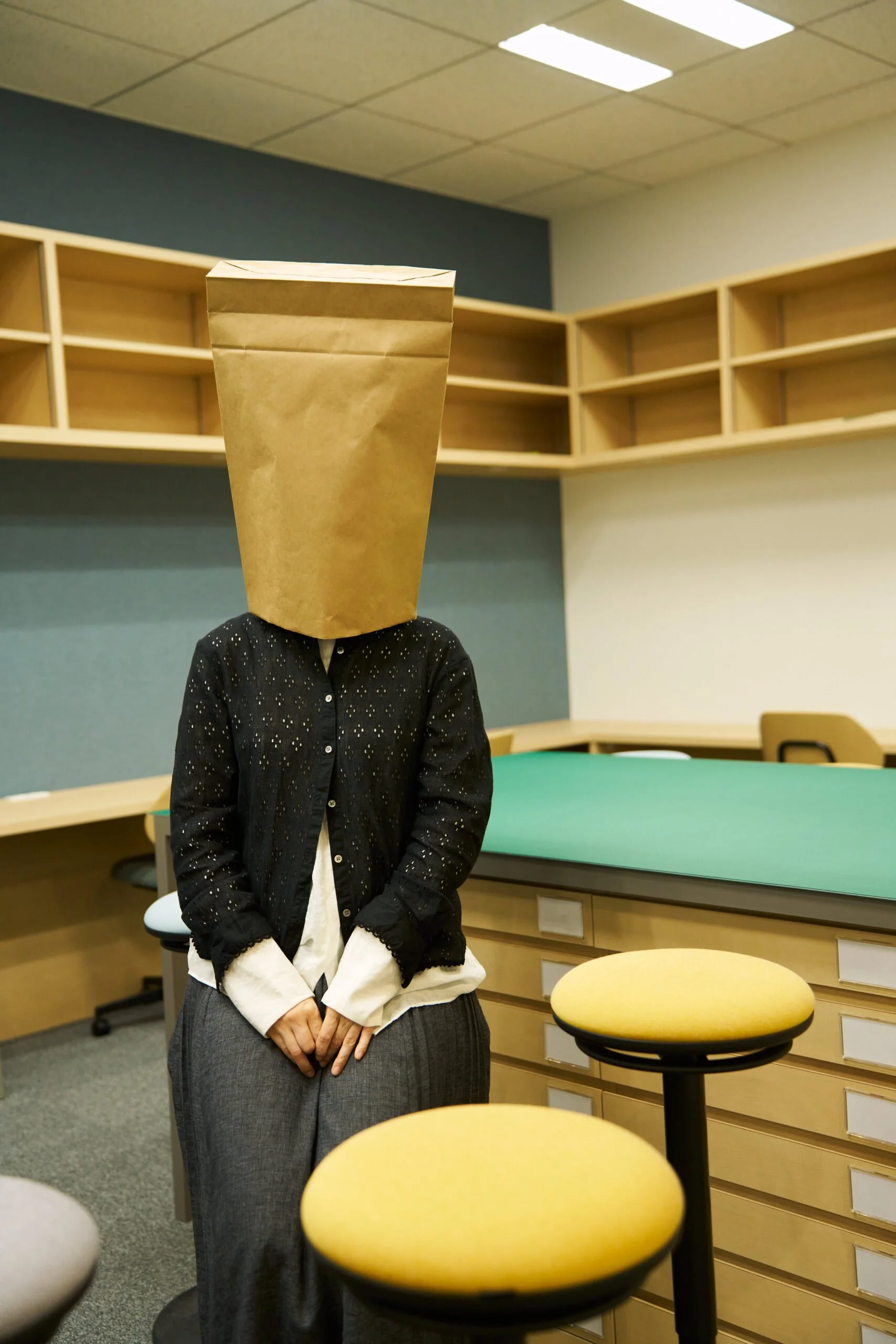 紙袋の袋を頭にかぶった人がオフィスの部屋に立っている