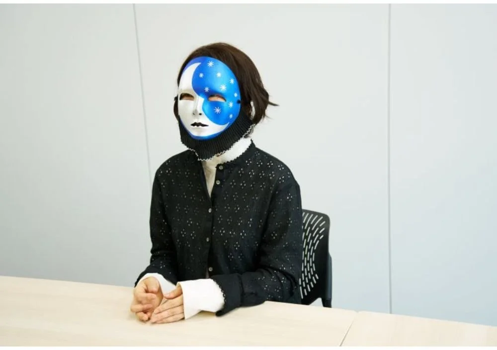 青と白の天体模様の仮面をつけた人が座っている