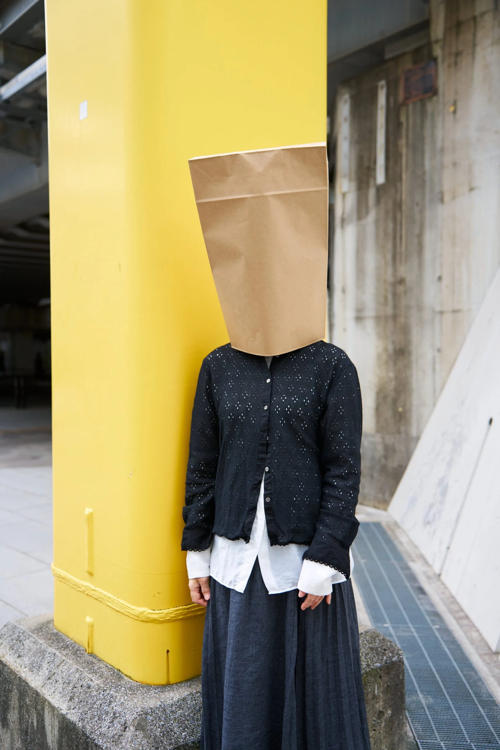 紙袋を頭にかぶった人が黄色い柱の横に立っている写真