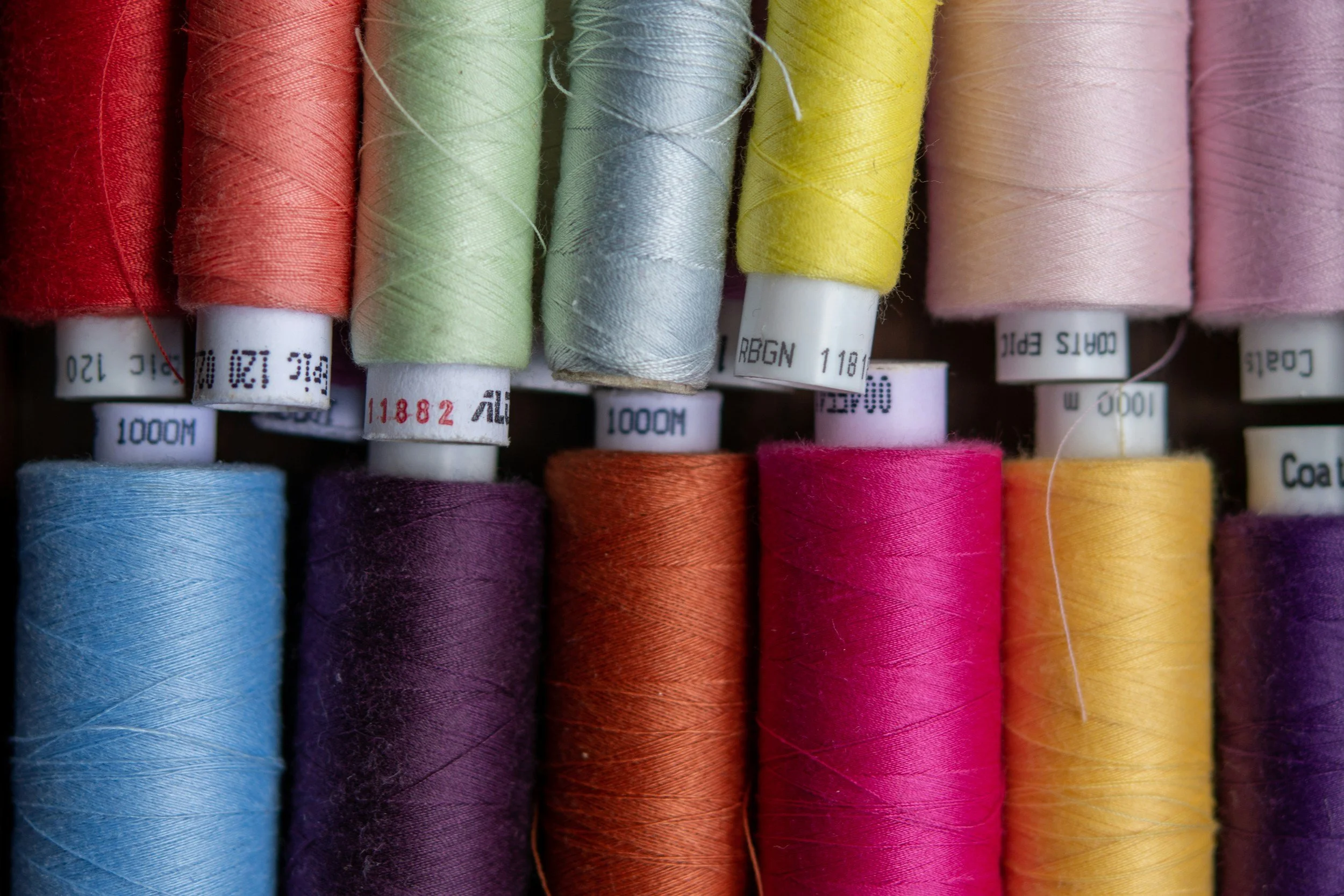 Spools of colorful sewing thread arranged in a row, including red, pink, green, gray, yellow, purple, blue, orange, and magenta.