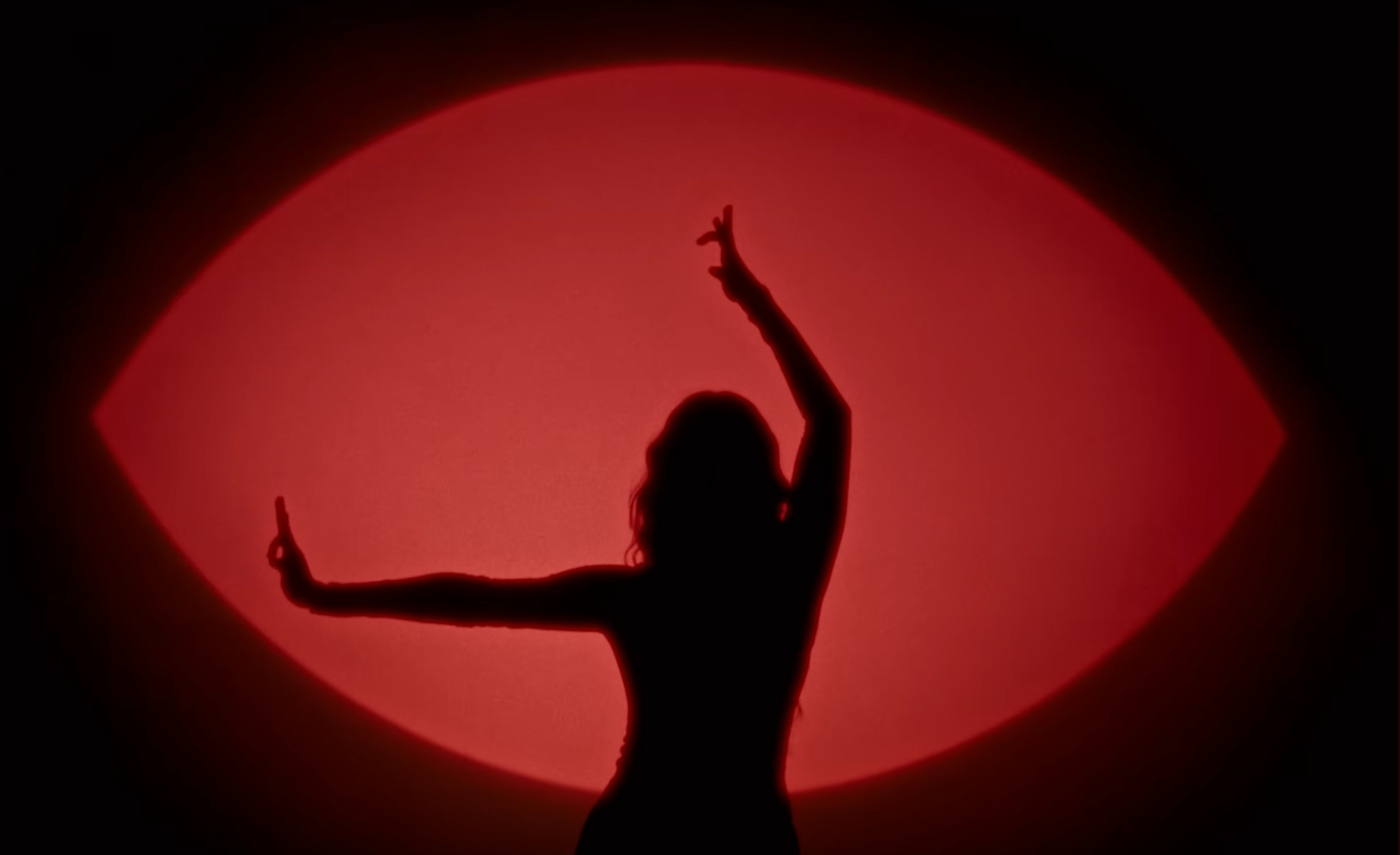 Silhouette of a woman with arms raised and outstretched in front of a large red illuminated background.