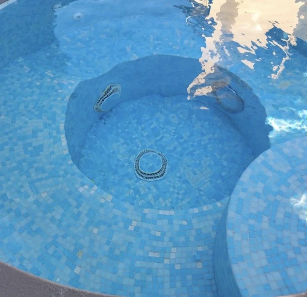 Close-up of a blue-tiled hot tub or pool with built-in jets and water reflections.