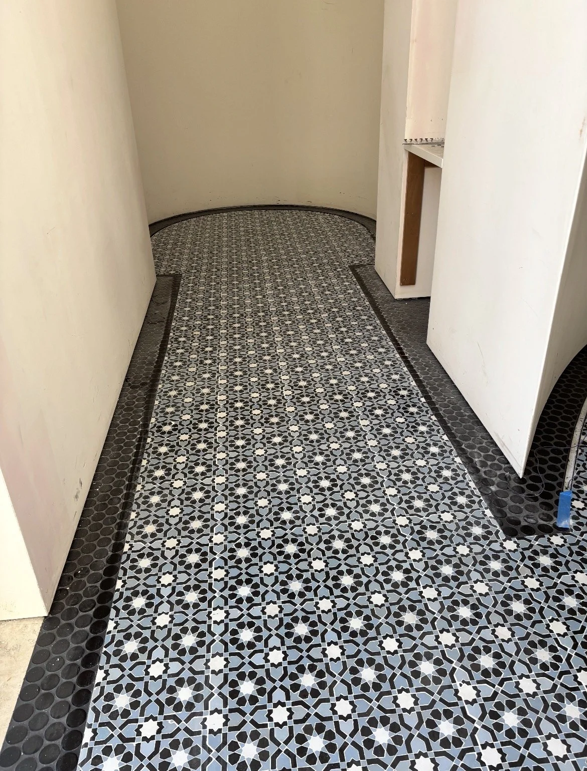 Close-up of a patterned floor with black and white tiles, leading into a small enclosed room with white walls.