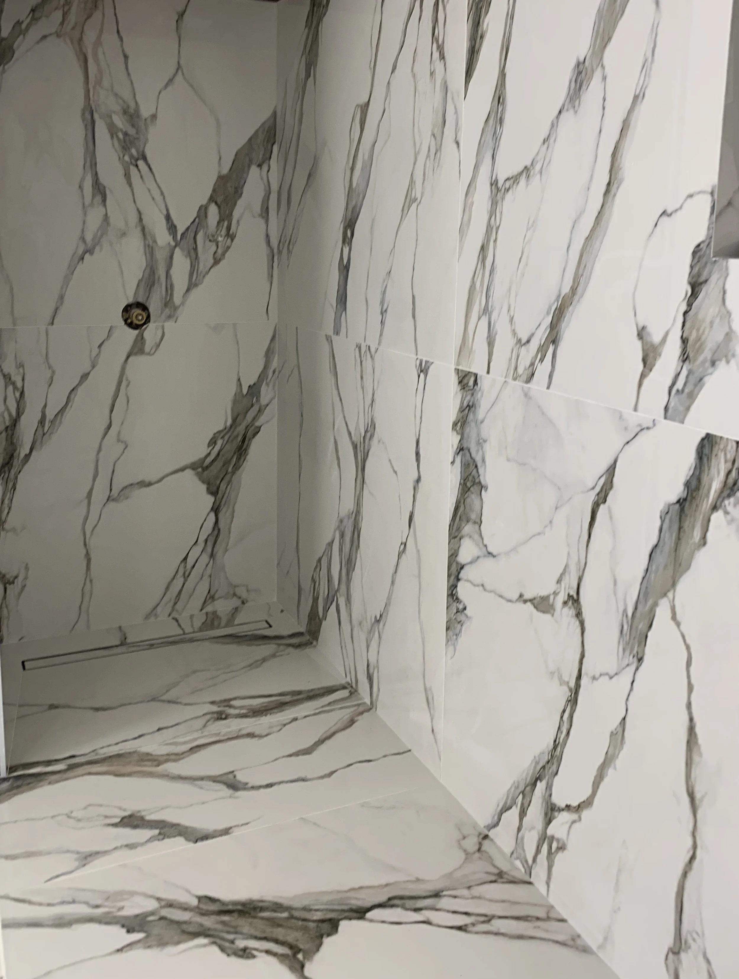 Marble-patterned bathroom shower walls and floor with a linear drain at the base of the corner.
