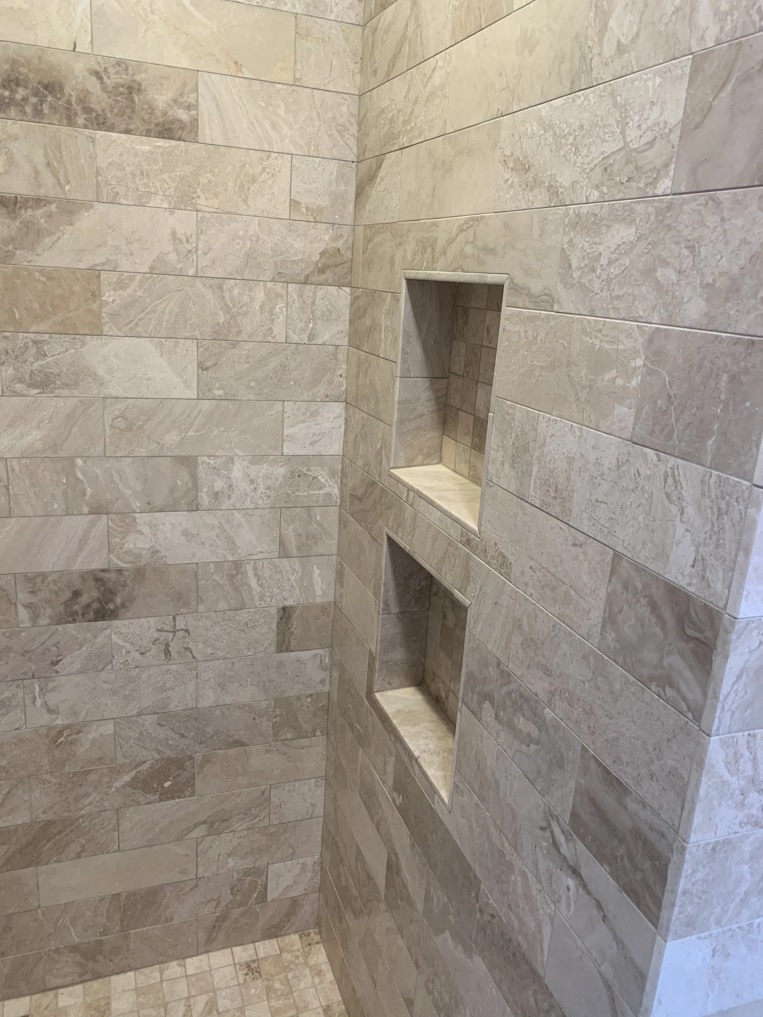 Close-up of a tiled shower wall with two recessed shelves.