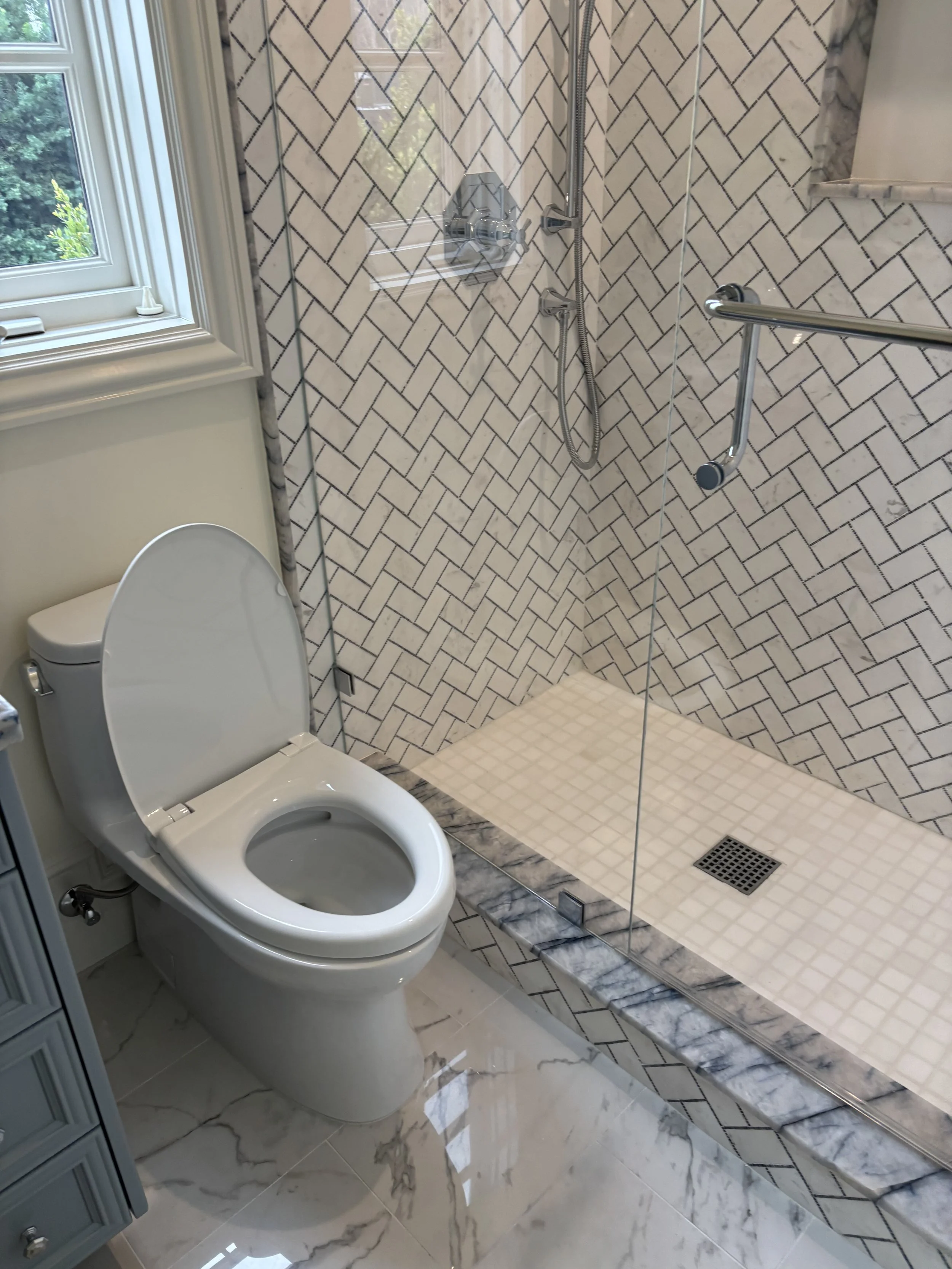 Bathroom with toilet and walk-in shower with glass enclosure, patterned tile walls, and marble floor.