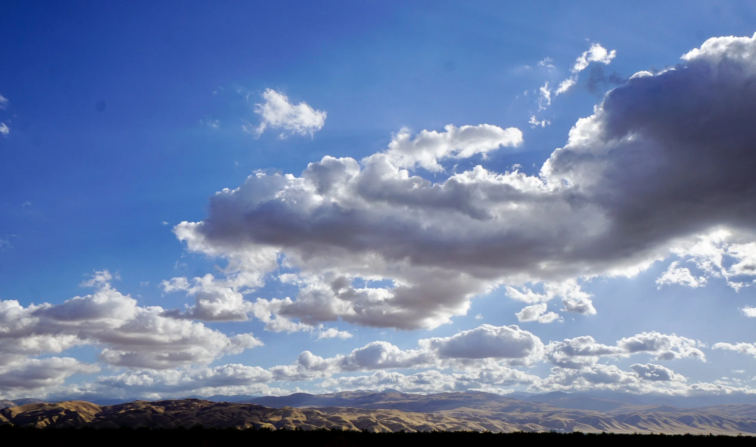 Wide view of a blue sky with white clouds over rolling hills.