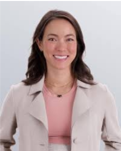 A woman with long dark hair smiling, wearing a light-colored jacket over a pink top against a plain gray background.