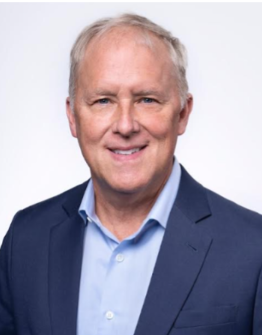 A portrait of a middle-aged man with gray hair, wearing a navy suit and light blue shirt, smiling against a white background.
