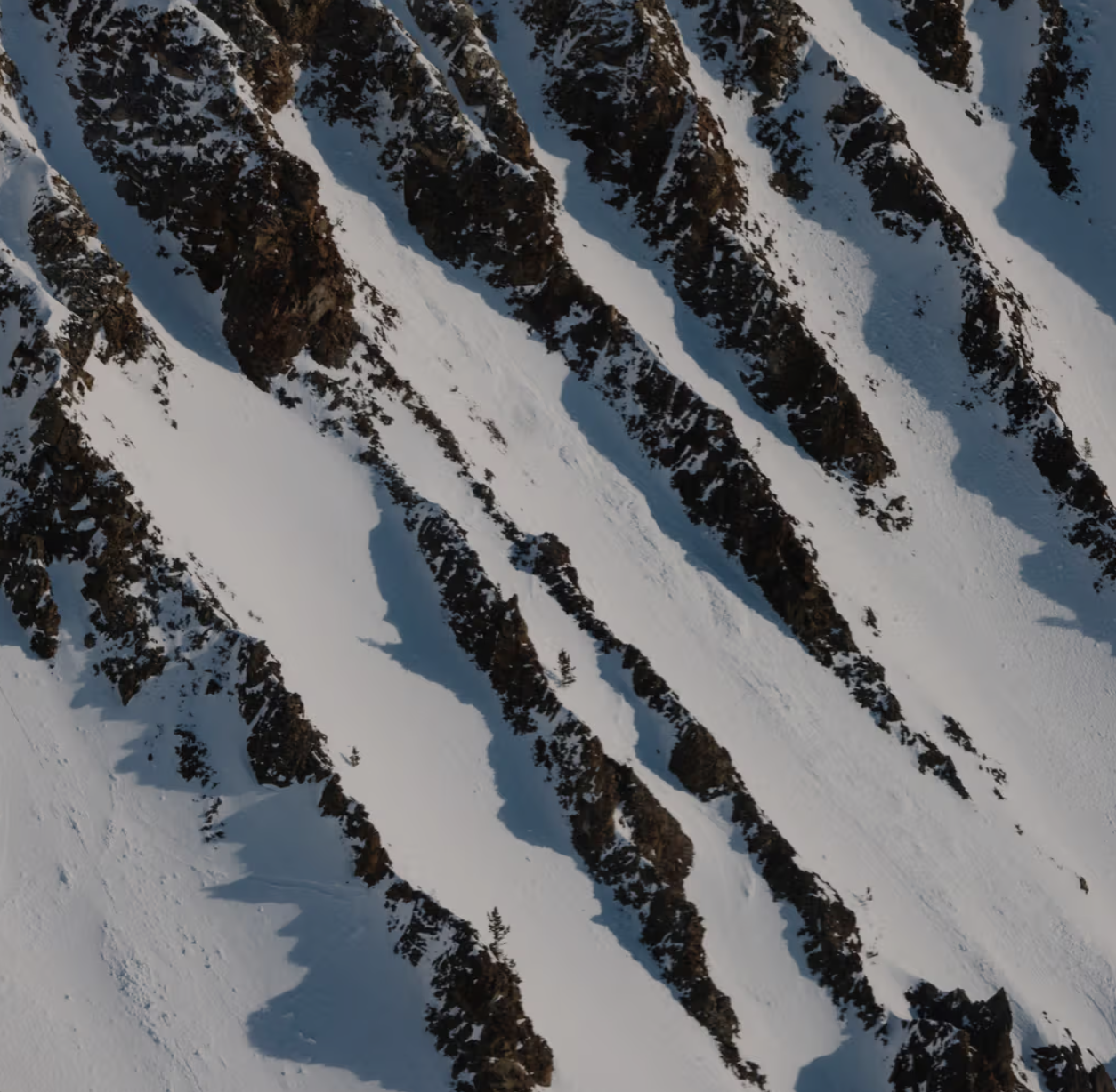 Snow-covered mountain slope with exposed dark rock formations creating sharp ridges.