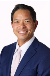 Professional portrait of a man wearing a navy blue suit and light-colored shirt, smiling against a white background.