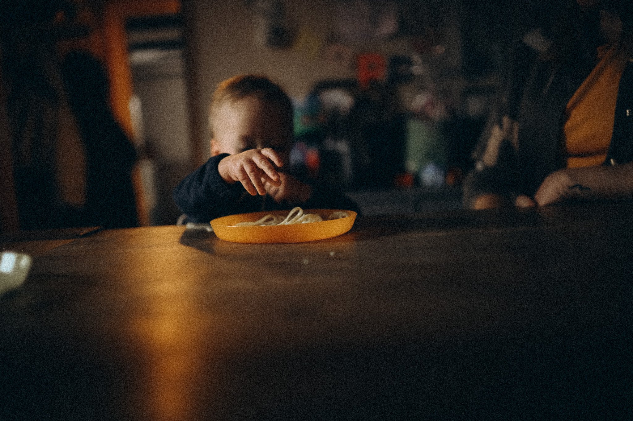 natürliche Familienfotografie in Kassel Kind greift nach den Nudeln am Tisch