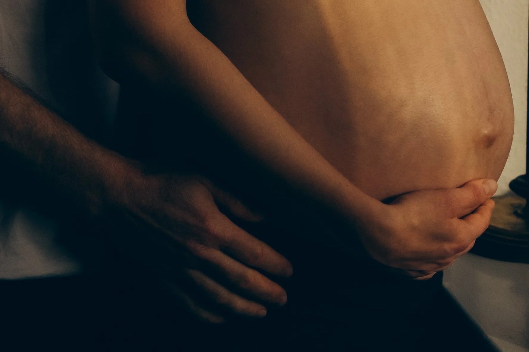 Nackt, obere Körperhälfte einer Frau mit einem Mann, Hände umfassen ihren Bauch und ihre Hüfte.