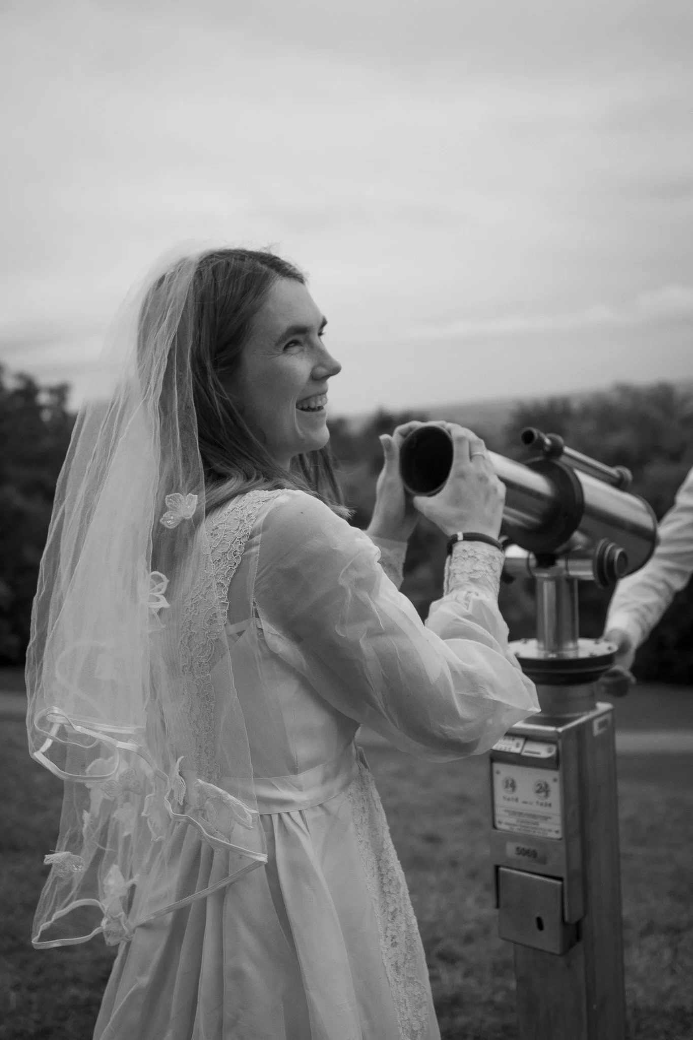 Eine Frau in einem weißen Kleid und Schleier schaut durch ein Teleskop im Freien.