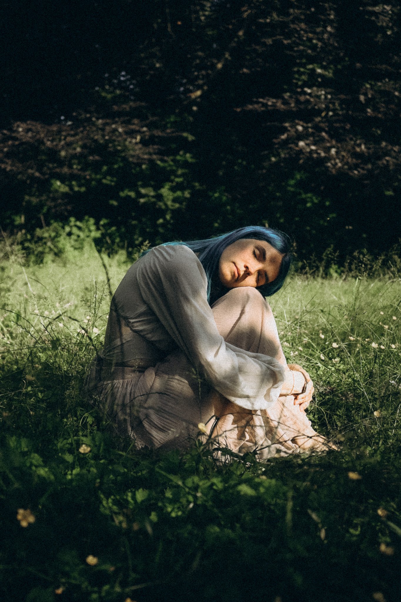 Eine Frau sitzt im Gras, hat die Augen geschlossen und wirkt entspannt in einer nächtlichen Umgebung.