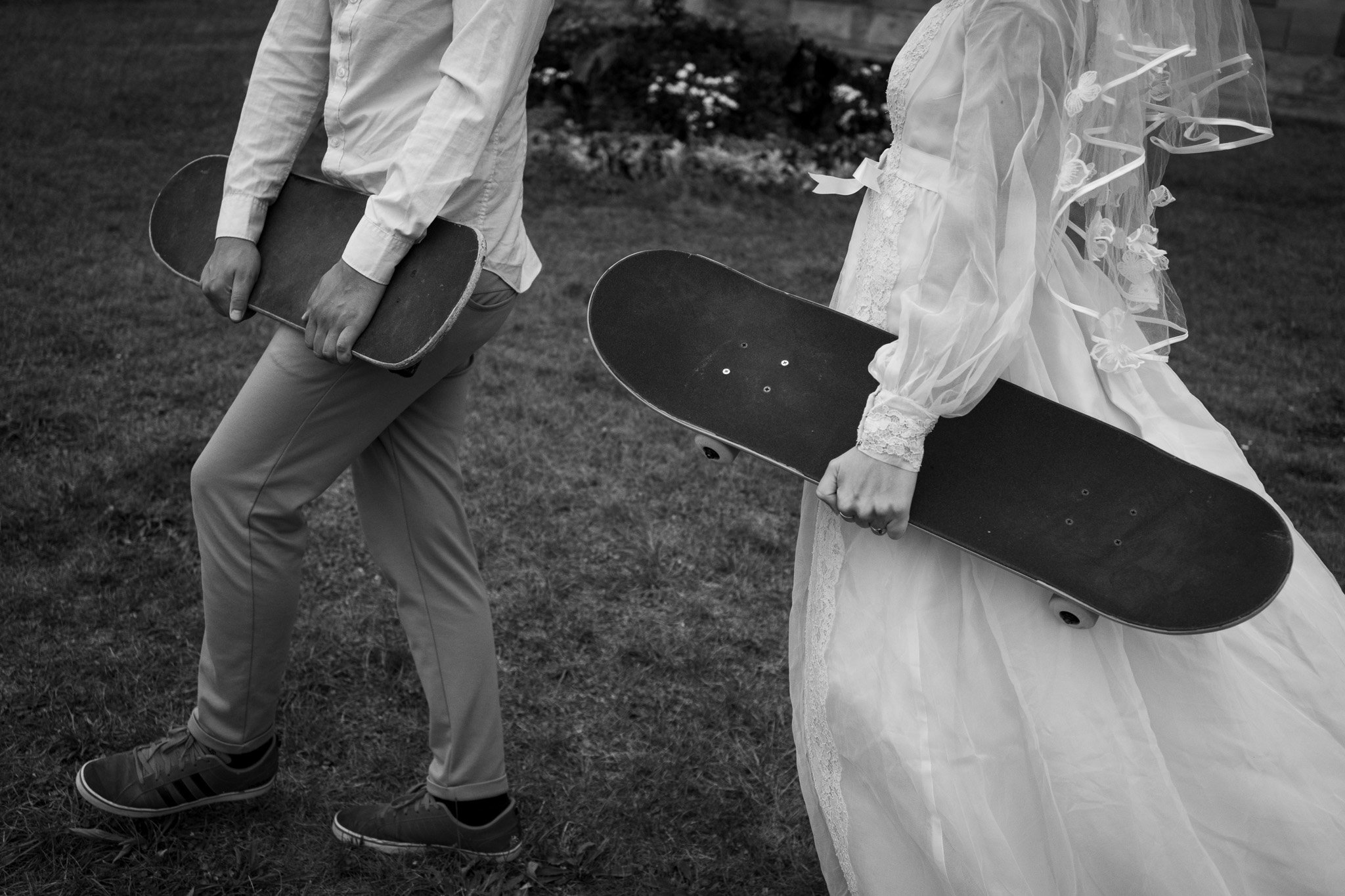 Zwei Menschen, einer in einem Anzug und eine in einem Brautkleid, stehen im Freien und halten Skateboards.