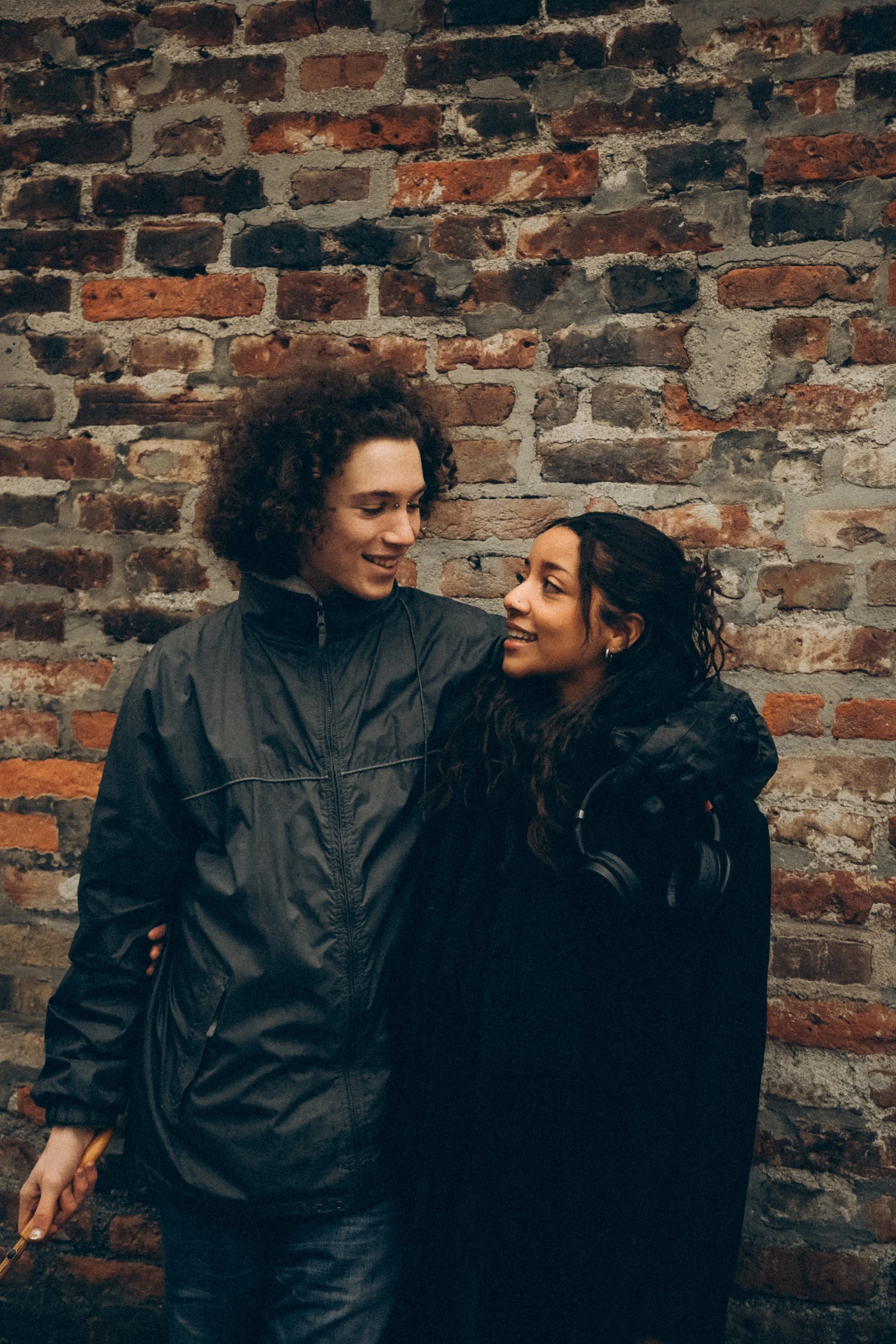 Ein Mann und eine Frau stehen sich nahe an einer Ziegelsteinwand, lachen und schauen sich an.
