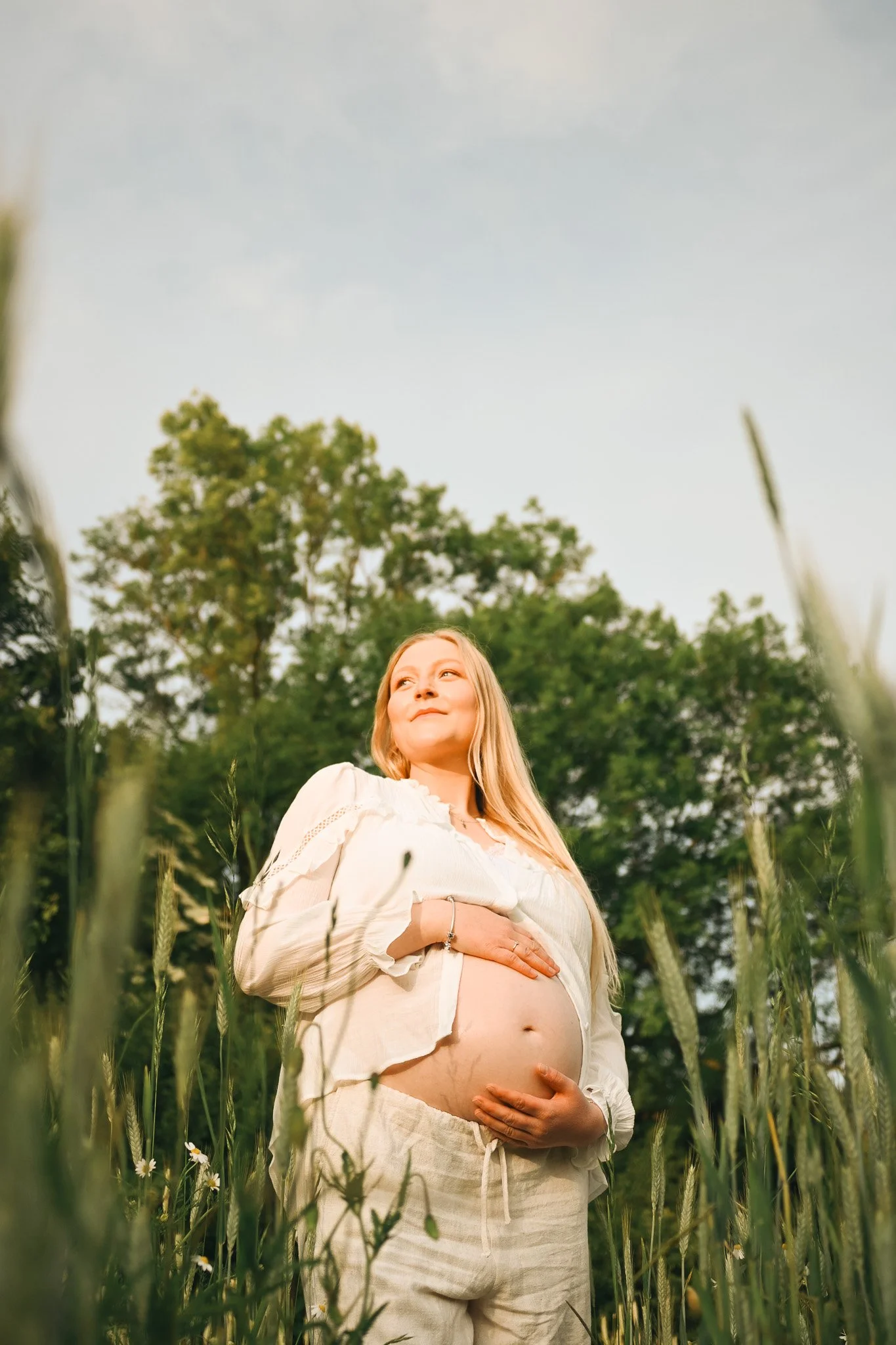 Schwangere Frau in einem weißen Kleid im Grünen bei Sonnenuntergang.