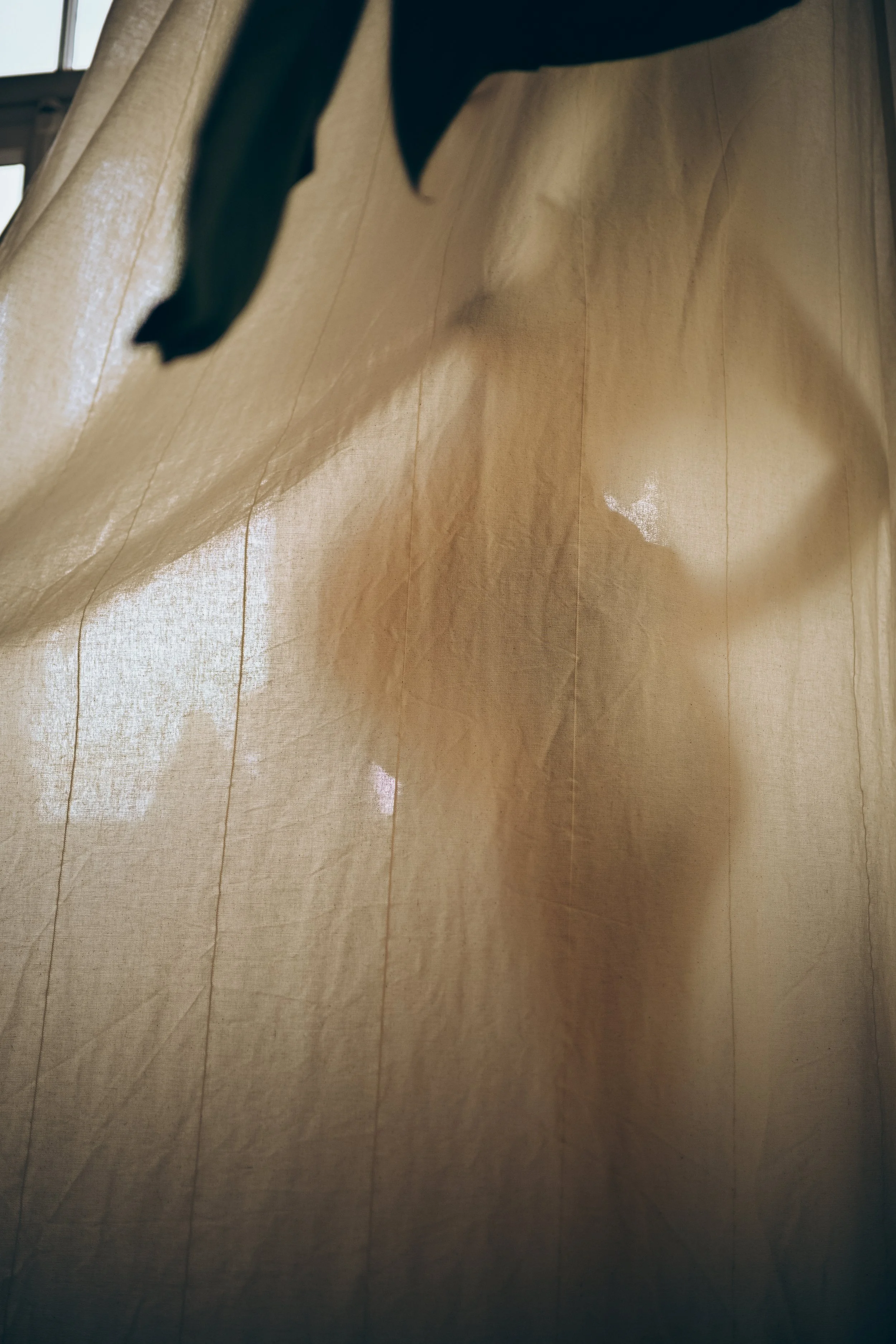 Ein Blick durch eine beige Stoffgardine, durch die schwach Licht und Schatten sichtbar sind.
