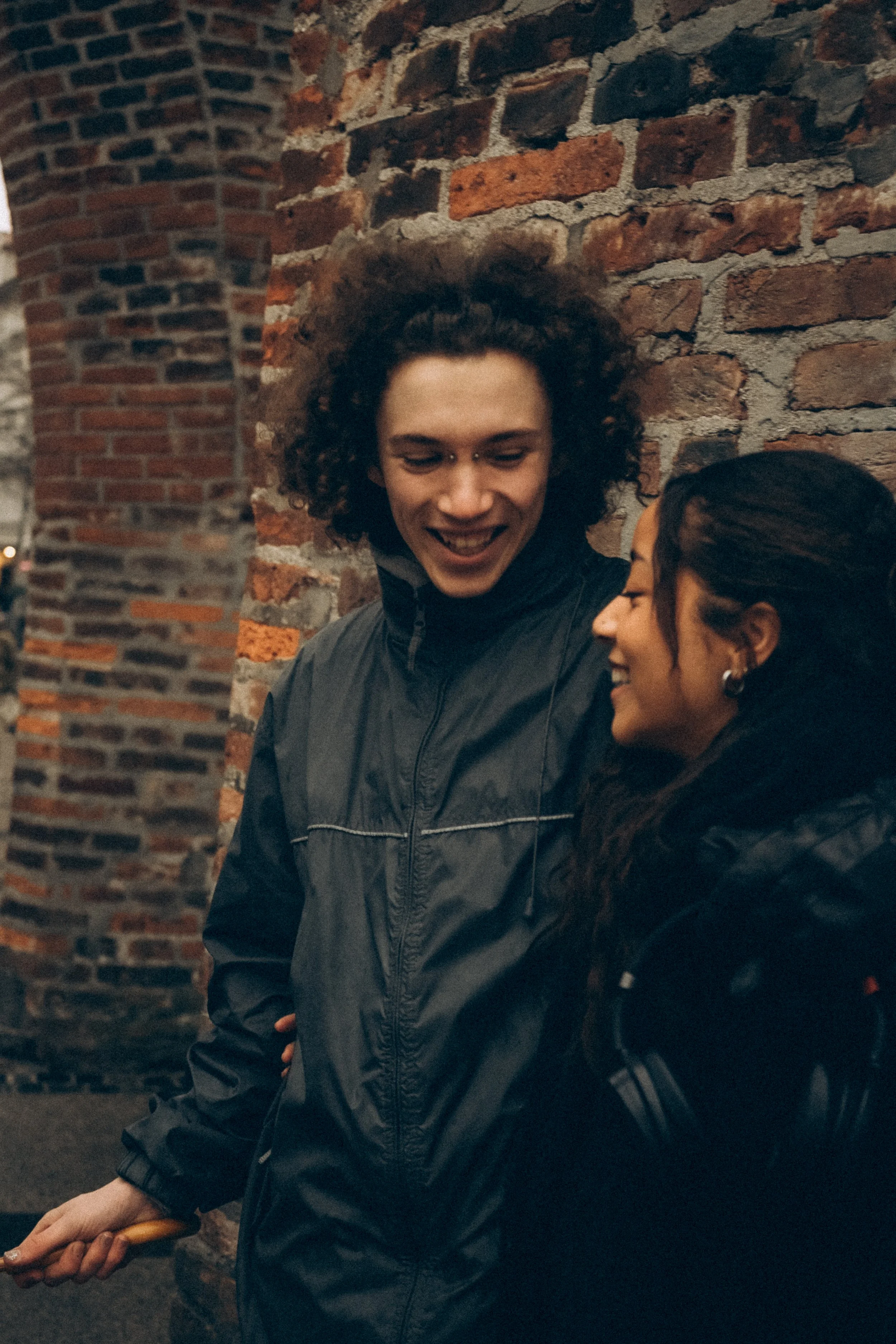 Zwei Menschen lachen und unterhalten sich, an einer brickernen Wand.