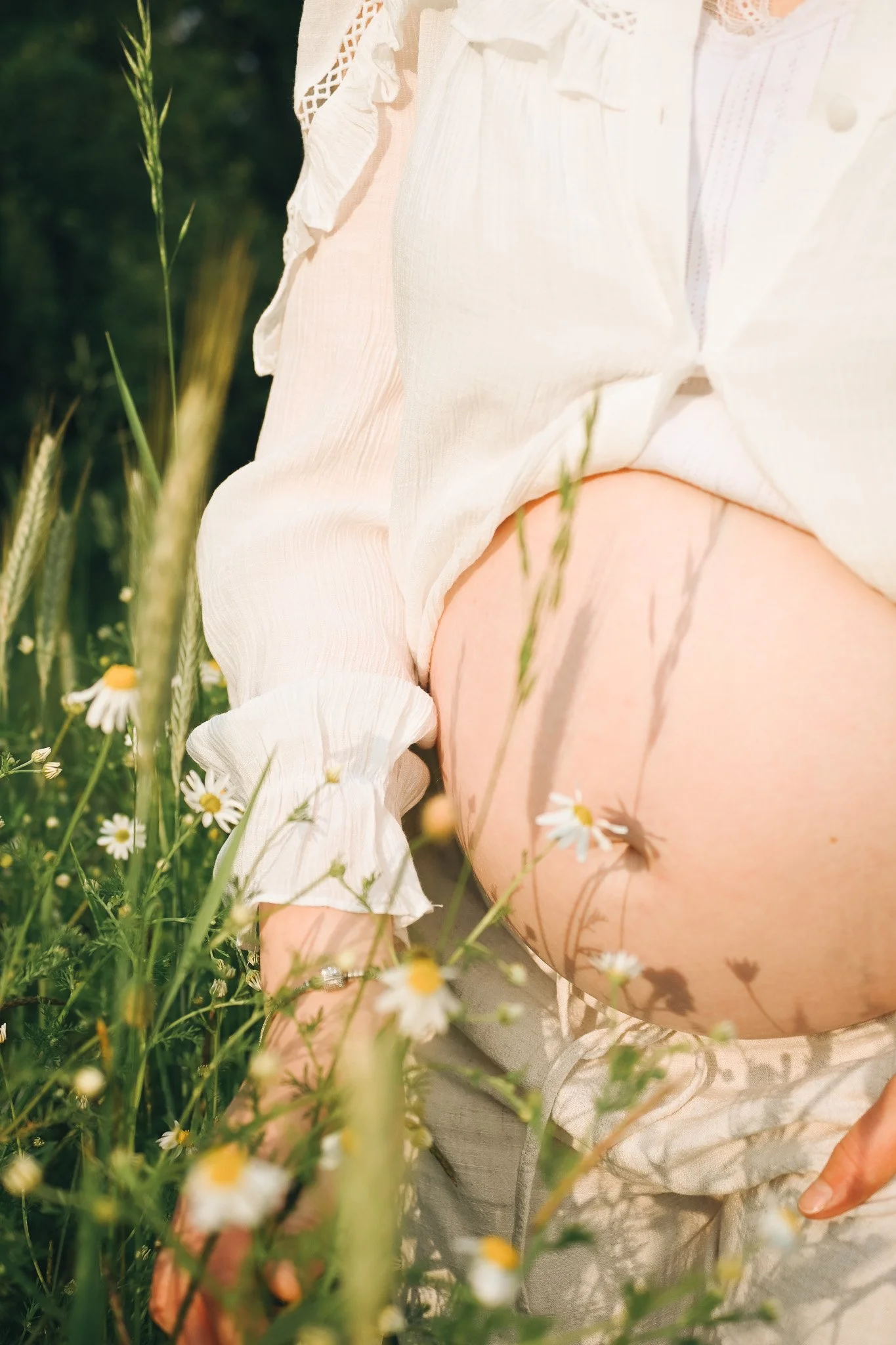 Nahaufnahme einer Person im weißen Kleid, die in einem Feld mit Gänseblümchen kniet.