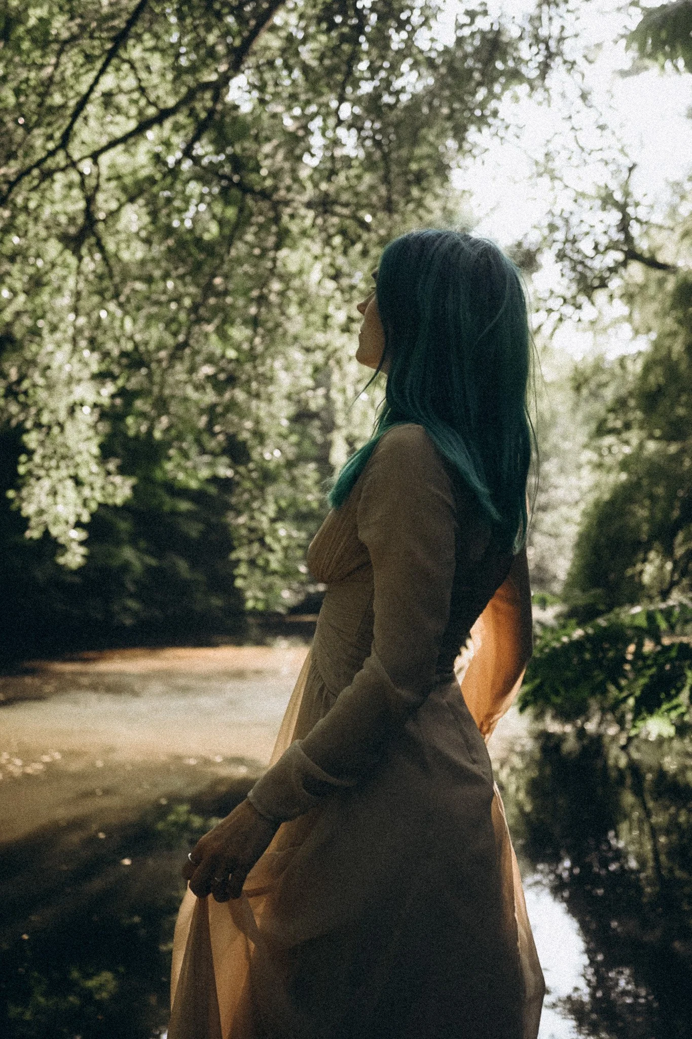 Eine Frau mit dunkelblauen Haaren, die in einem Wald am Fluss steht.